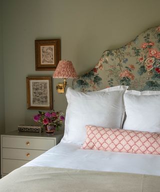 neutral bedroom with floral headboard, white bedding and pink cushions and wall sconce