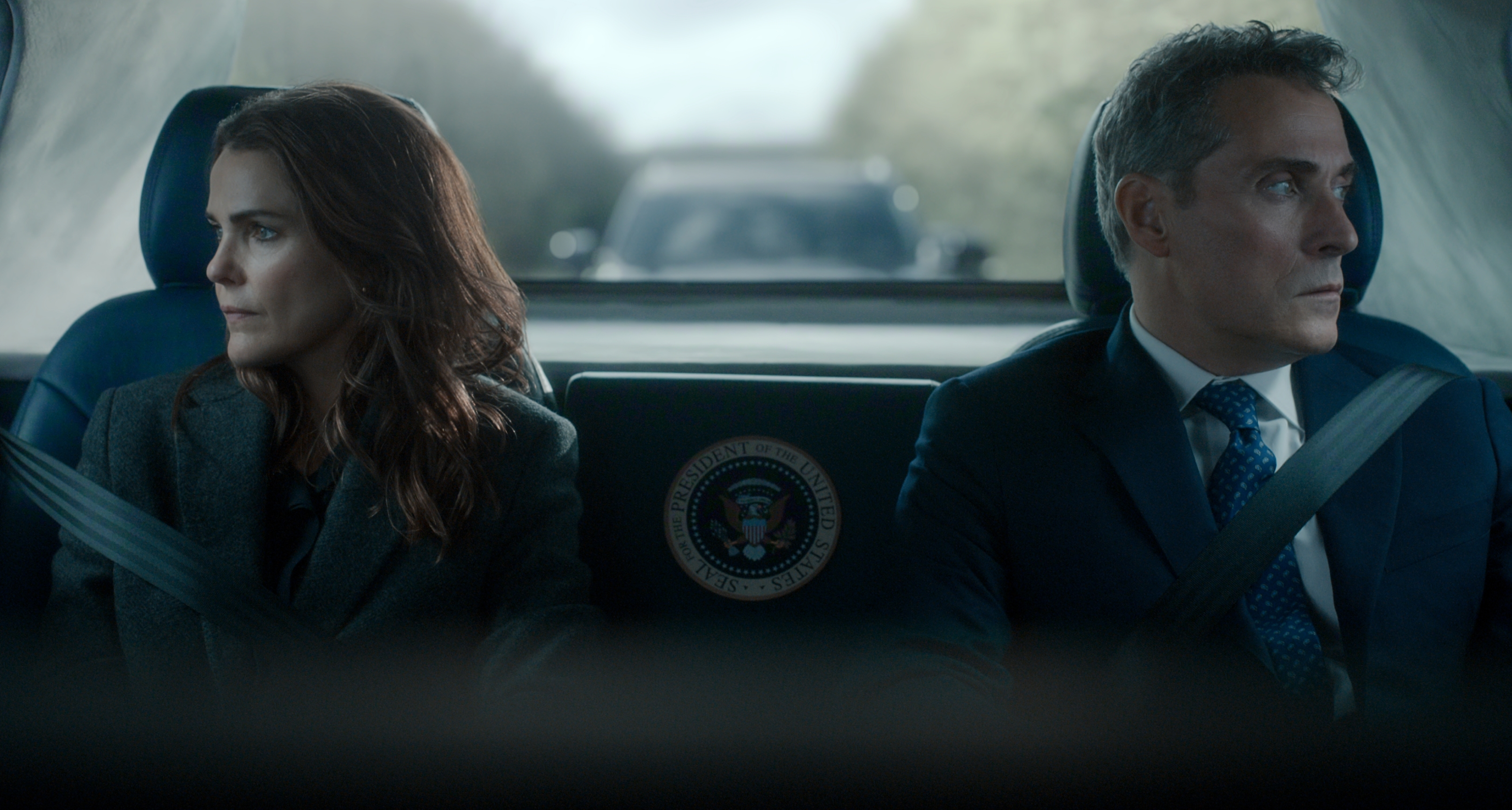 Keri Russell as kate wyler and rufus sewell as Hal Wyler sitting in the back of a car looking in different directions out of the windows in the diplomat season 4