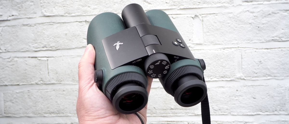 Swarovski Optik AX Visio binoculars held in a hand in front of a white wall