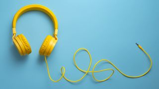 A pair of yellow headphones on a light blue background with the wire trailing
