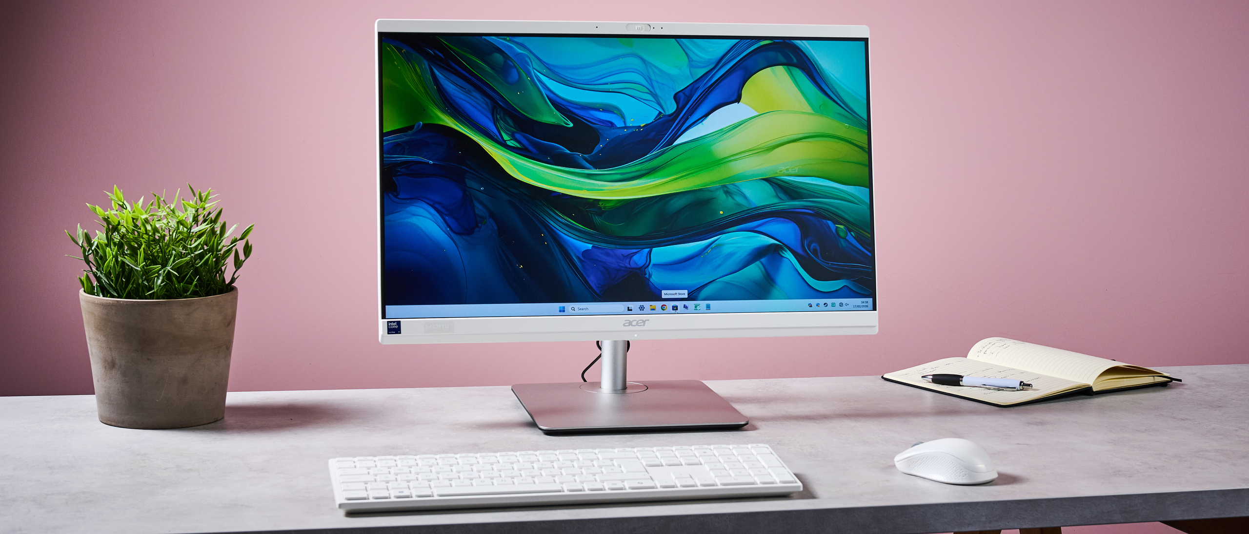 Acer Aspire C24 on desk with plant and note pad, against a pink background