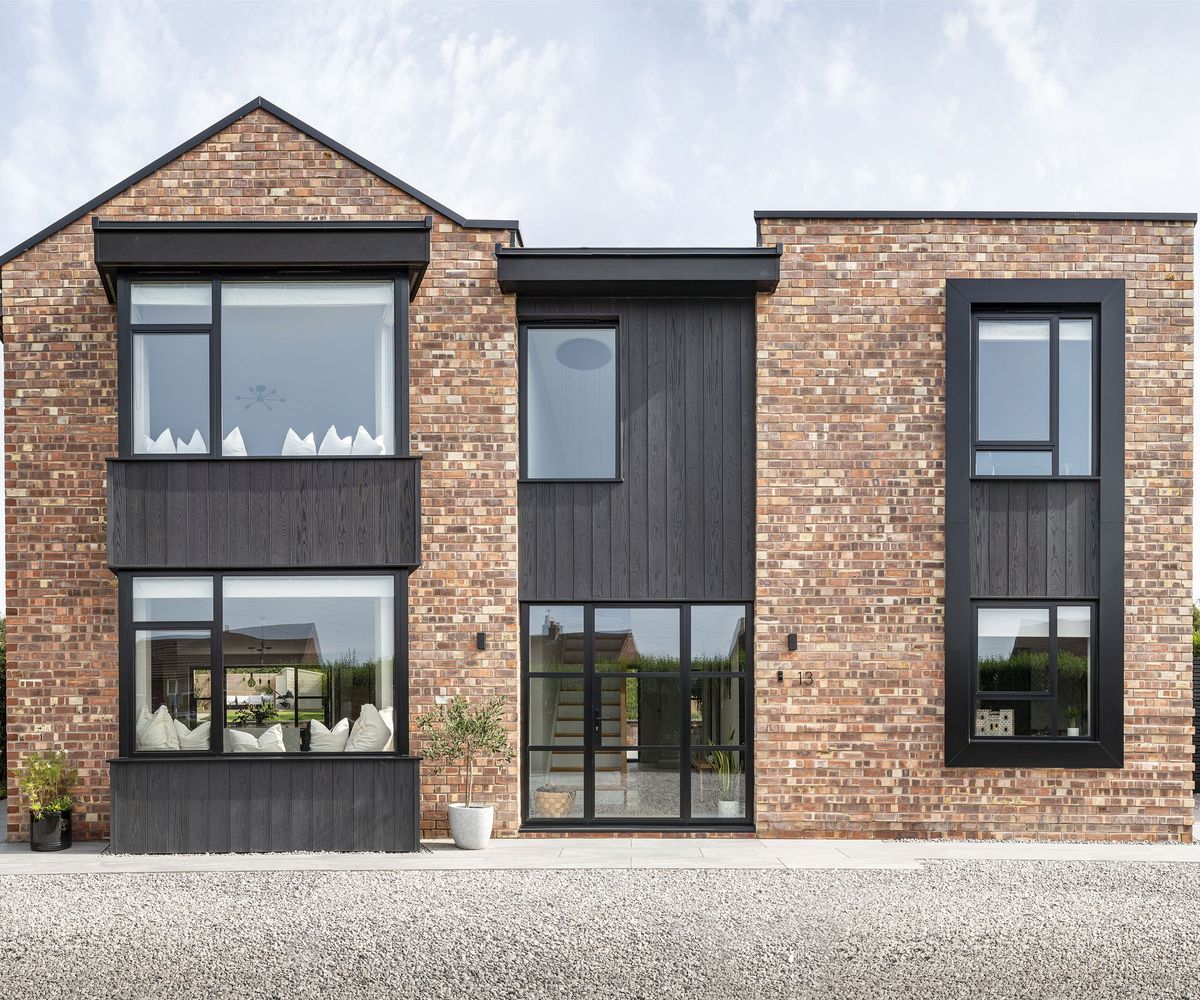 The front exterior of a newly renovated house. The cladding is a mixture of red brick and timber. There is large contemporary glazing on both of the two storeys. One section of the home has a pitched roof whilst the other is flat.