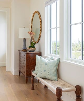 A coastal-style entryway with large windows, a bench and an antique dresser