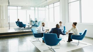 Four smiling business people sitting round a table in a well lit room with two of them shaking hands