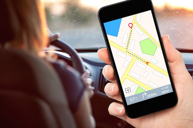 A woman holds a smartphone displaying a map inside a car.