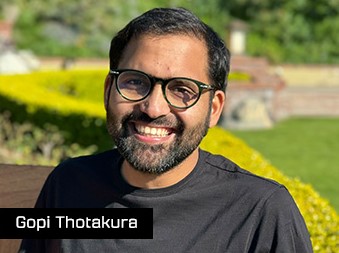  a bearded man with dark hair and glasses in a black shirt. 