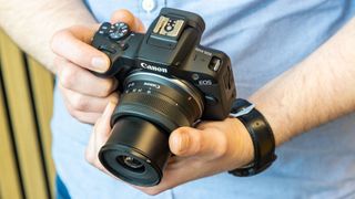 Canon EOS R100 camera being held by the reviewer