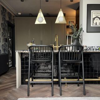 Black kitchen island with pendant lights next to green and black wallpaper wall