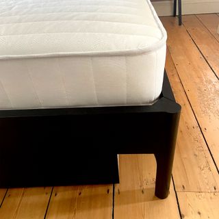 The corner of the Dreams Workshop Follows Traditional Spring Mattress in a black bedframe with wooden floorboards underneath