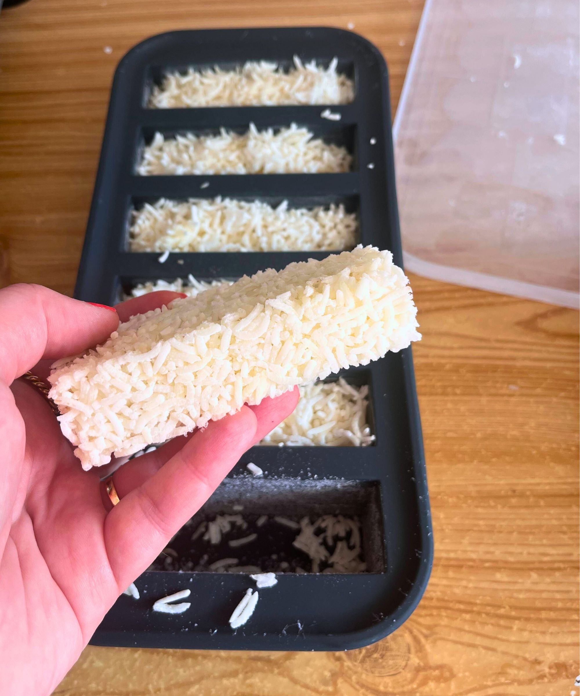 A block of frozen white rice is being held in the photo, showing the block freeze method with a Souper Cube silicone mold, with the rest of the batch in the background on a kitchen counter