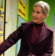 Duchess Sophie wearing a maroon dress and coat pressing a button on a wall