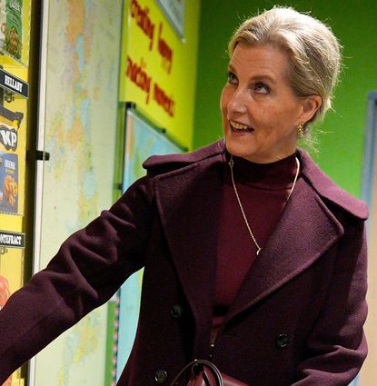 Duchess Sophie wearing a maroon dress and coat pressing a button on a wall