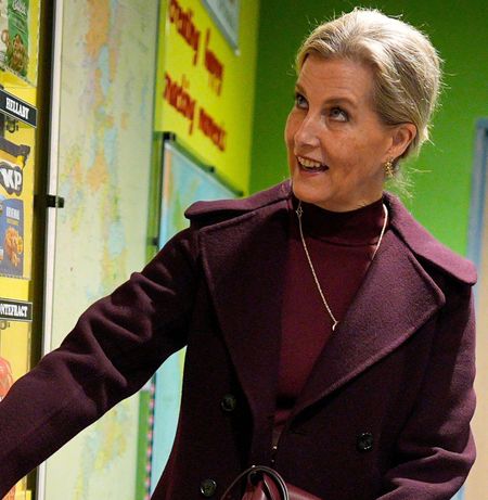 Duchess Sophie wearing a maroon dress and coat pressing a button on a wall