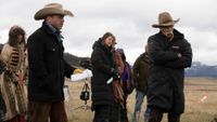 Taylor Sheridan holding paper and Sam Elliott crossing his arms behind the scenes of 1883.
