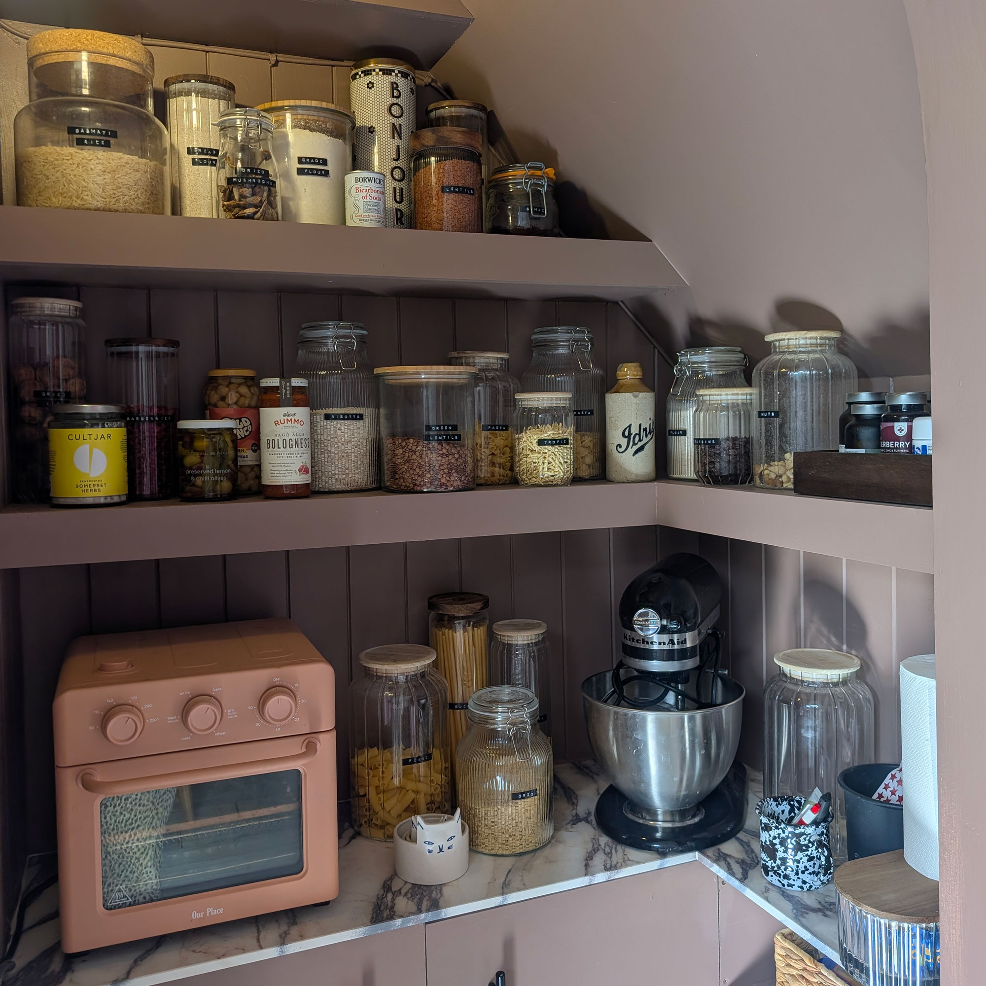 Corner of pantry painted in grey-pink shade with shelves full of glass storage jars, Wonder Oven and KitchenAid mixer
