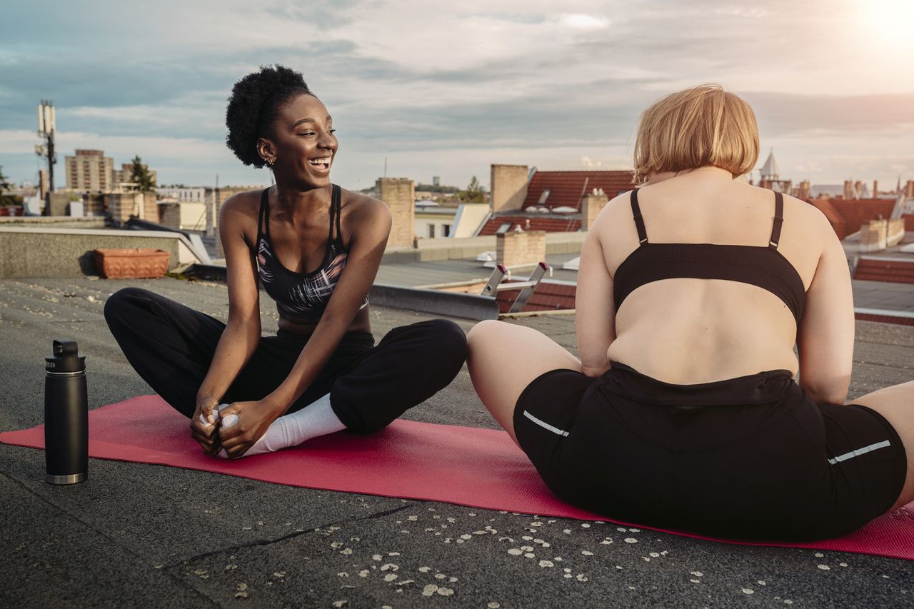 Smiling female friends exercising on rooftop, morning yoga, best time to do yoga