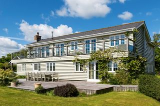 cream-painted wooden-clad home with full width balcony and decking with blue skies