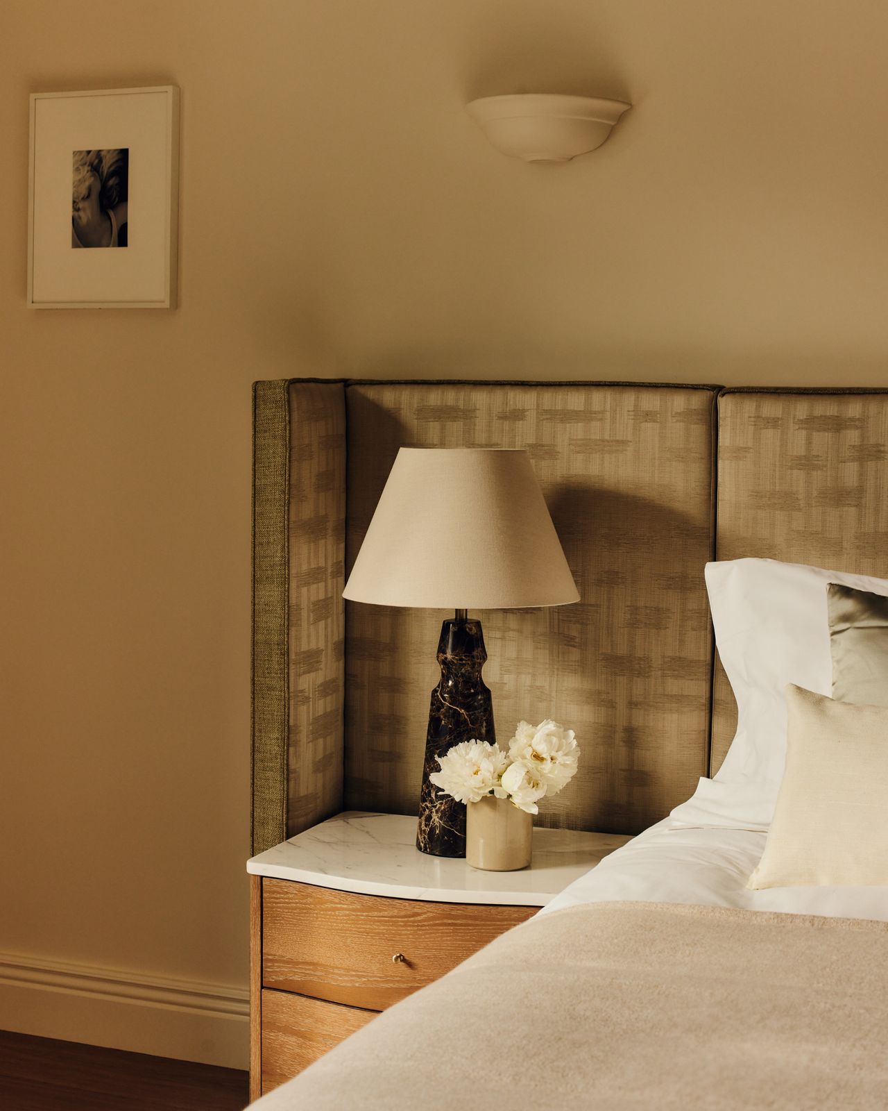 Detailed photo of the guest bedroom with an upholstered headboard and bedside table. It features photography by Gabby Laurent and a bespoke winged headboard