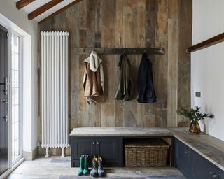 A kitchen with a mudroom nook with blue-grey boot bench and reclaimed oak paneled walls