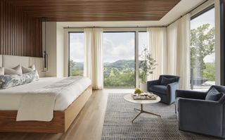 A bedroom with wooden slatted walls, large floor-to-ceiling windows, and two blue arm chairs