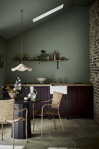 sage green kitchen with walls and ceiling painted, flagstone floor, rattan chairs, eggplant cabinetry, exposed brick wall, wood countertops