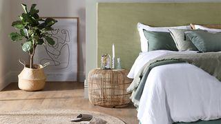 Japandi bedroom with sage green wall, low bed and woven beside table