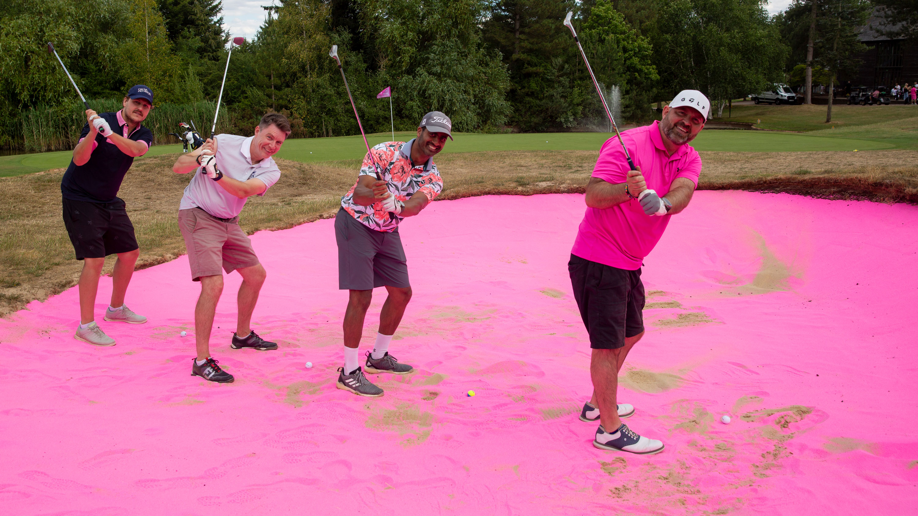 four golfers hitting from pink sand at a charity golf day