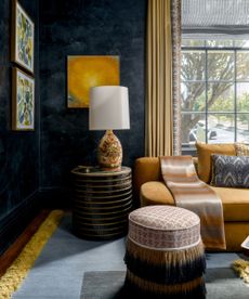 A sophisticated living room corner featuring dark, textured navy walls contrasted by a plush mustard yellow sofa and gold drapes.