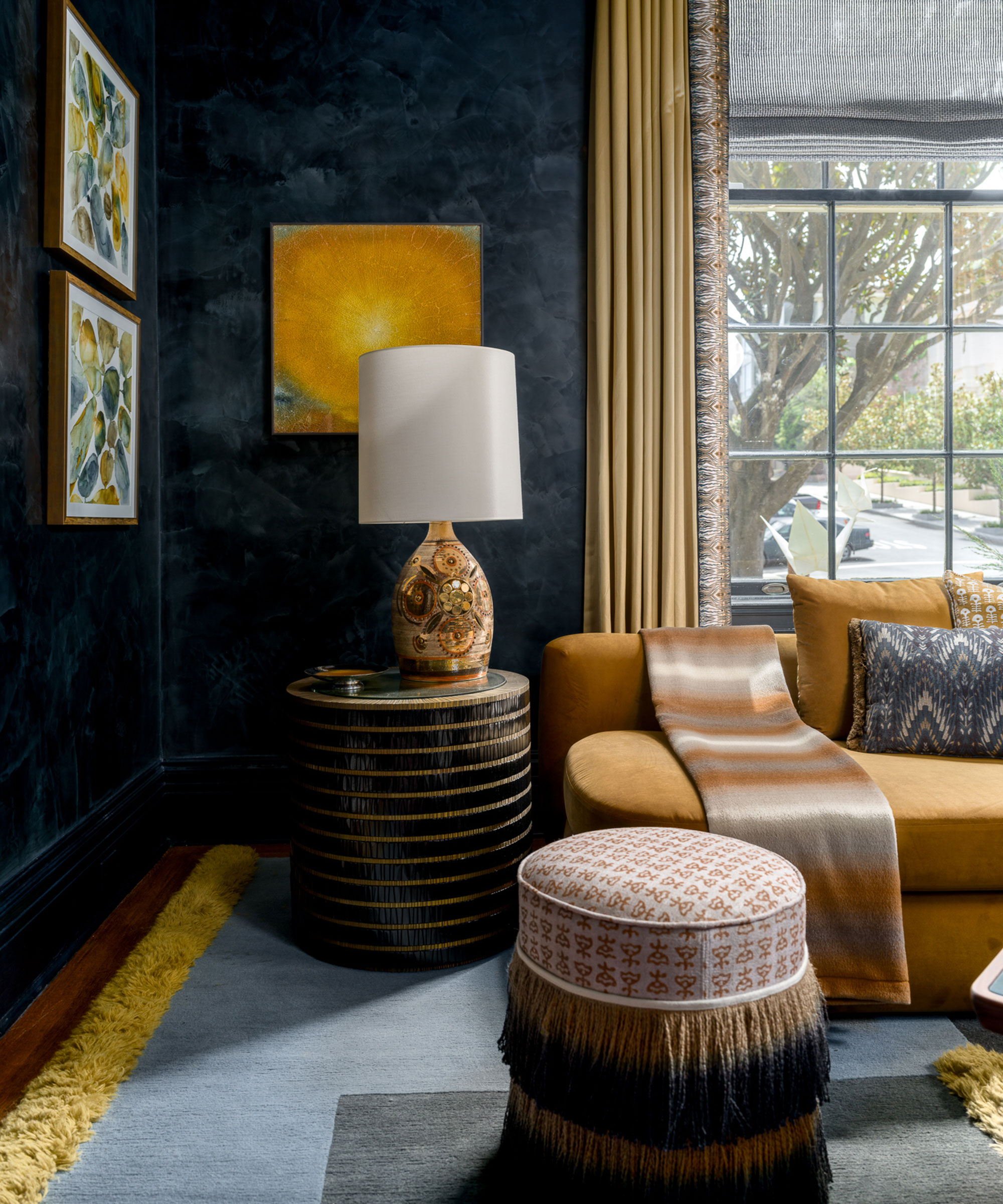 A sophisticated living room corner featuring dark, textured navy walls contrasted by a plush mustard yellow sofa and gold drapes.