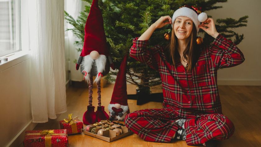 A young woman wearing tartan Christmas pajamas and a Santa hat decorates a Christmas tree. 