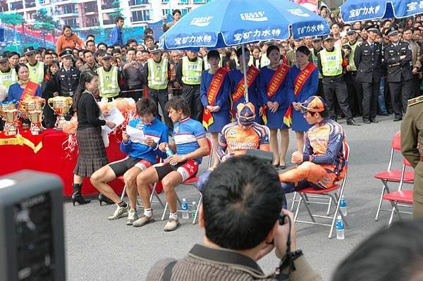 Riders wait for the podium ceremony after stage 2. Joe Papp and Derek Wong are seated to the right.