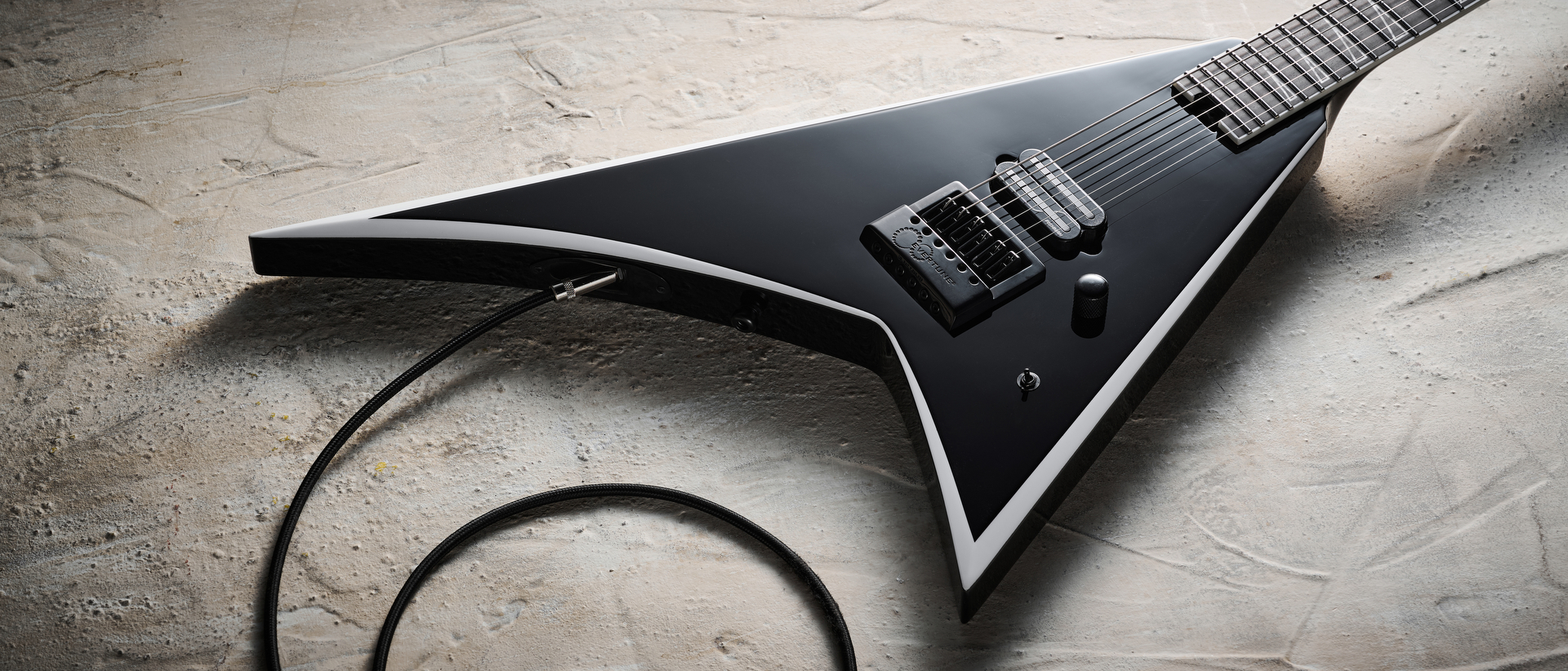 A Jackson Pro Plus Series Signature Christian Andreu Rhoads RR24 EVTN6 electric guitar lying on a distressed white floor with a guitar cable plugged into it