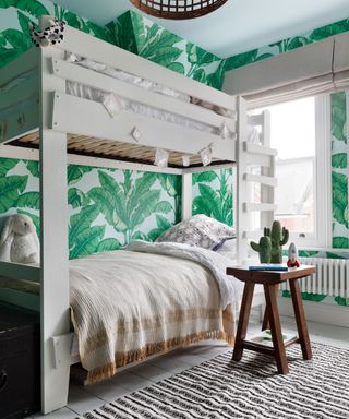 Kids shared bedroom ideas illustrated by a white bunk bed and large botanical-print green wallpaper.