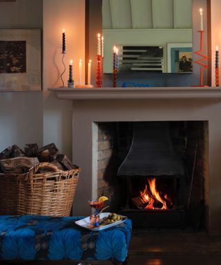 cozy fall living room with candles lit on mantel, log burner, log basket, ottoman, mirror, artwork