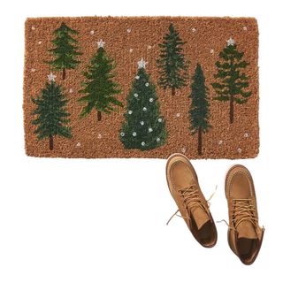 A festive doormat with Chritstmas trees and snow, with two brown, lace-up shoes to the bottom right