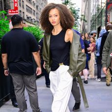 Nico Parker wearing a black tank top, green leather jacket, and white pants in NYC
