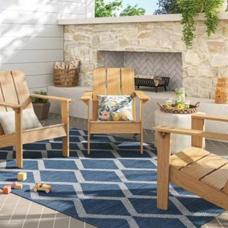 An outdoor patio setup with wooden armchairs and a dark blue patterned rug