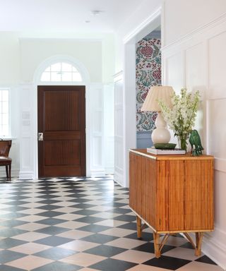 Large entryway with tiled flooring, bamboo style sideboard, white painted walls, sideboard decorated with table lamp, flowers and ornaments