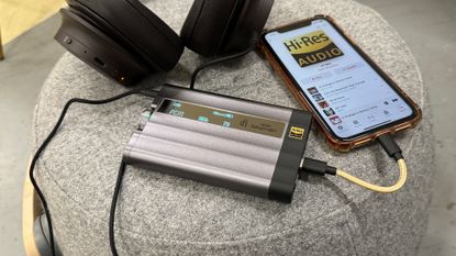 The iFi xDSD Gryphon on a stool next to a pair of headphones and phone