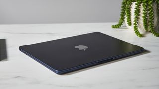 Bästa laptop: En svart Apple MacBook Air (M2, 2022) ligger stängd på ett vitt marmormönstrat skrivbord i en studio med en grön krukväxt i bakgrunden.