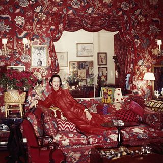 A woman in a red outfit , sitting on a red printed sofa with matching decor in the room.