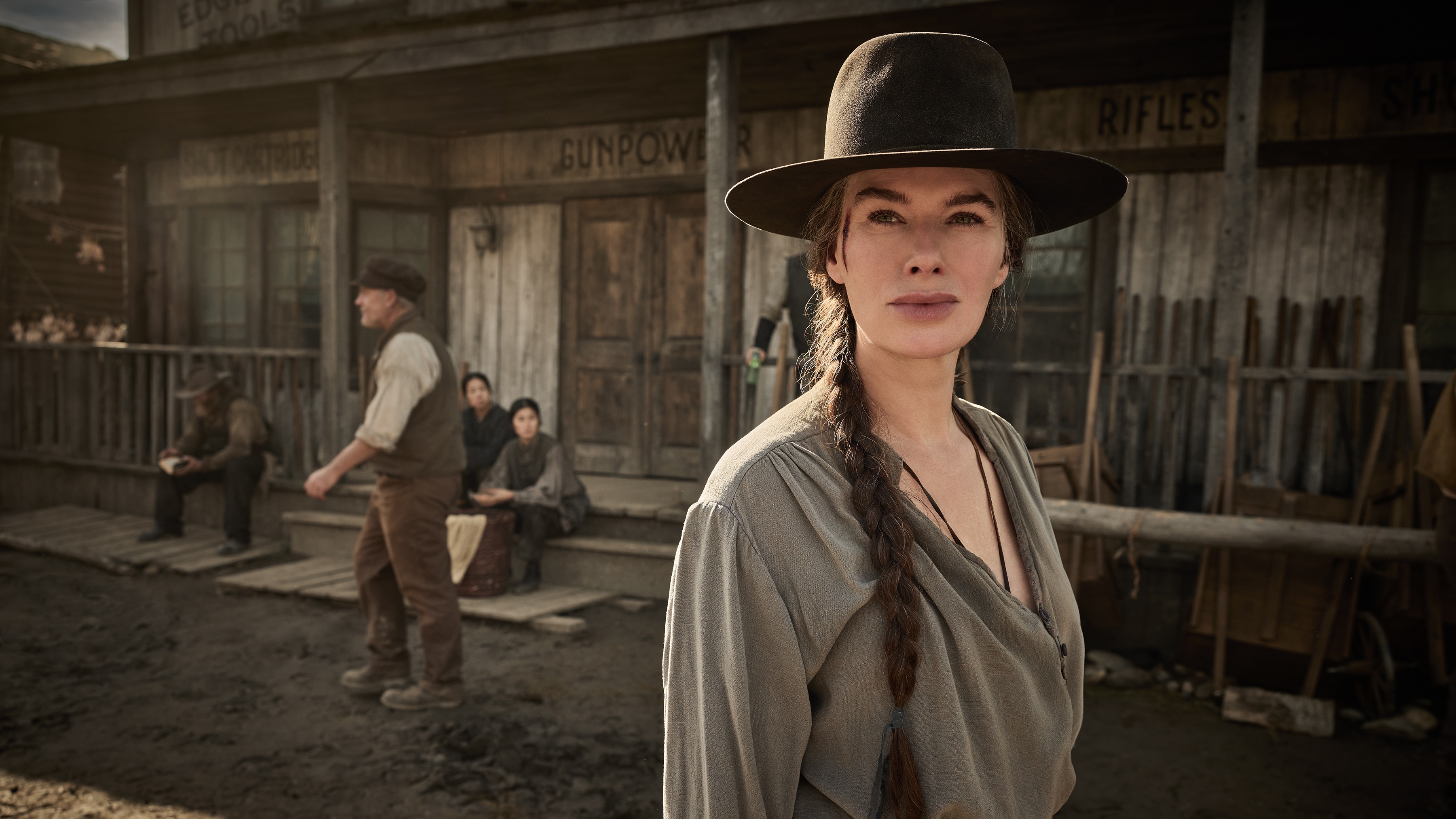 Lena Headey as Fiona Nolan wearing a black cowboy hat and her hair in a plait with a western building behind her.