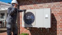 Man in hard hat leaning against an air source heat pump