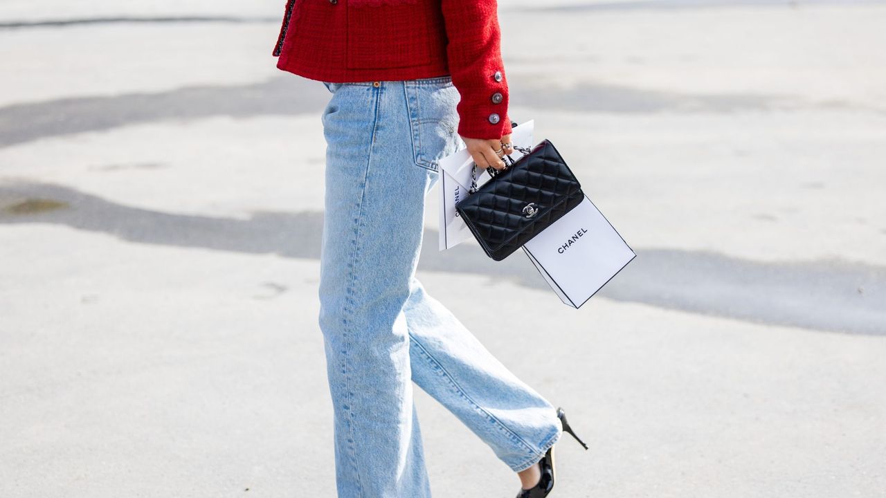 A woman wearing jeans, crossing the road, holding a beauty hall perfume, Chanel carrier bag 