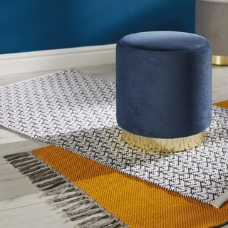A pair of Aldi rugs overlapping one another on a white wooden floor with a short blue upholstered stool sat on top.
