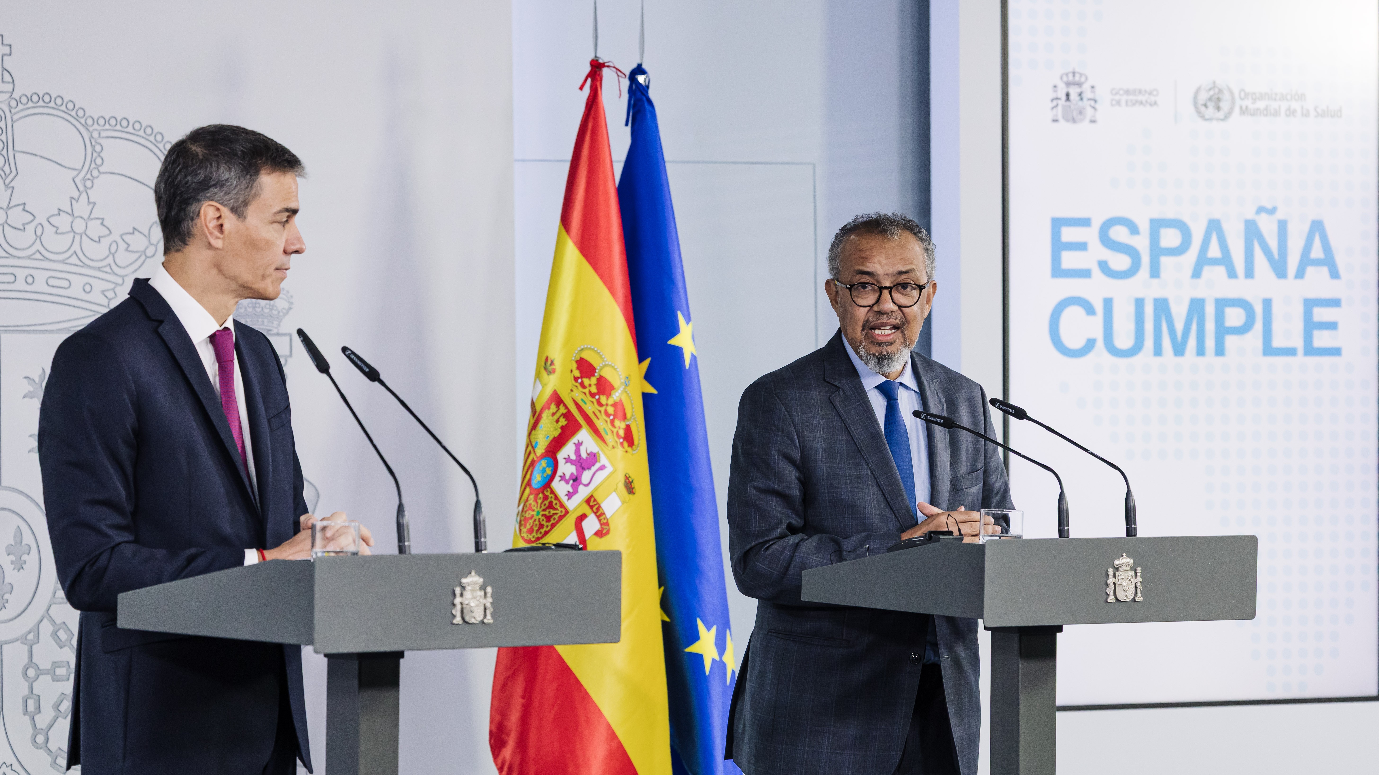 Two men stand at separate podiums behind the flags of Spain and the European Union.