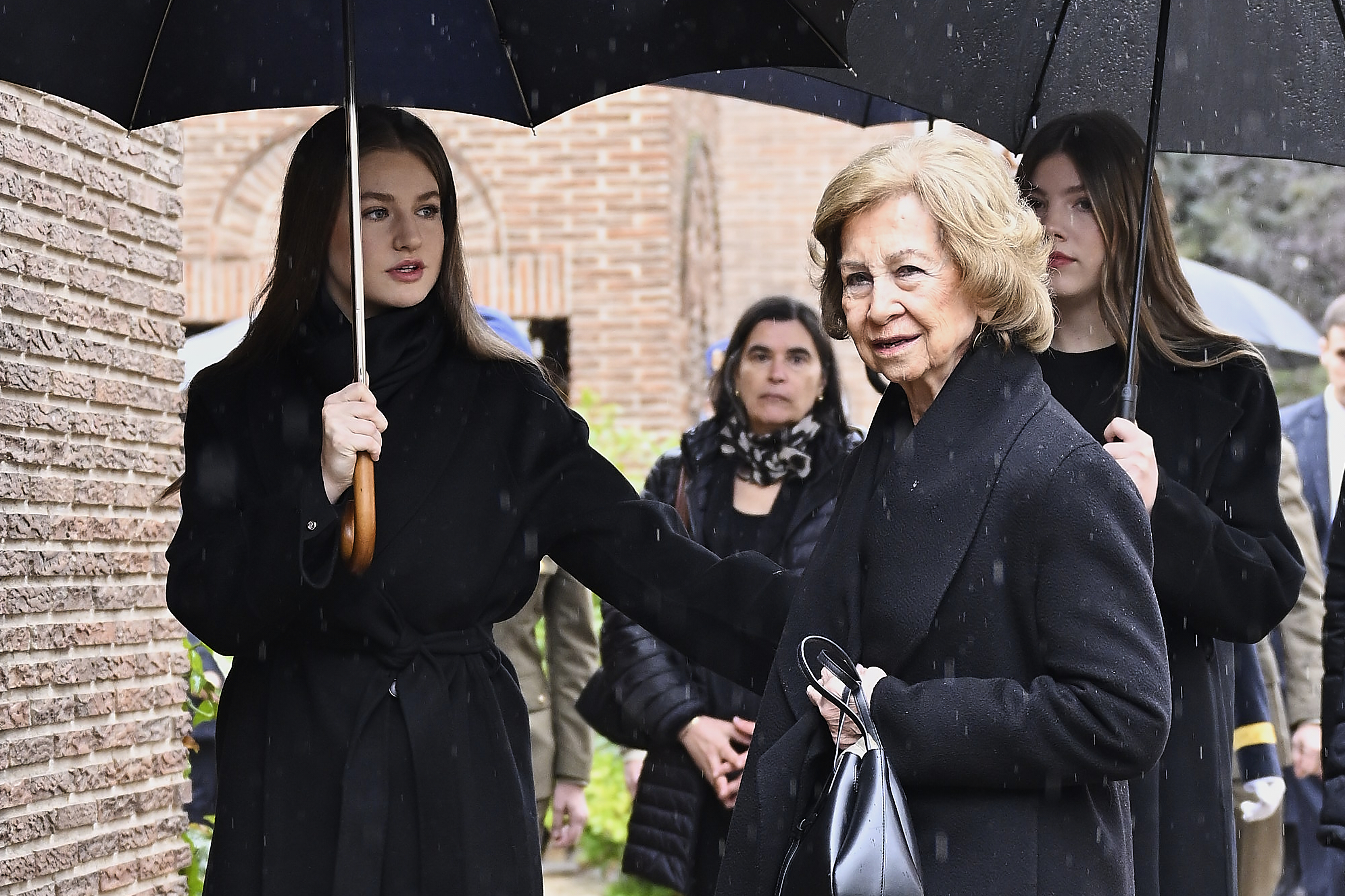 Princess Leonor and Princess Sofia holding umbrellas next to Queen Sofia