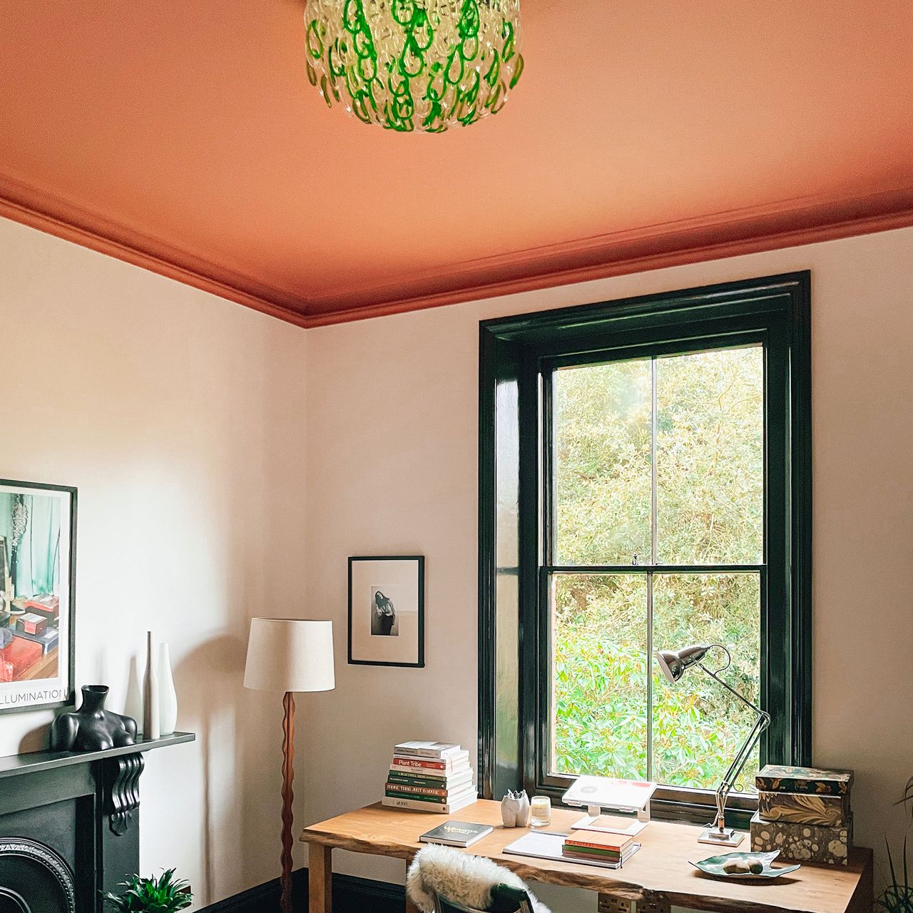 Home office with desk, decorated with white walls, black window frame, terracotta ceiling and green and glass chandelier