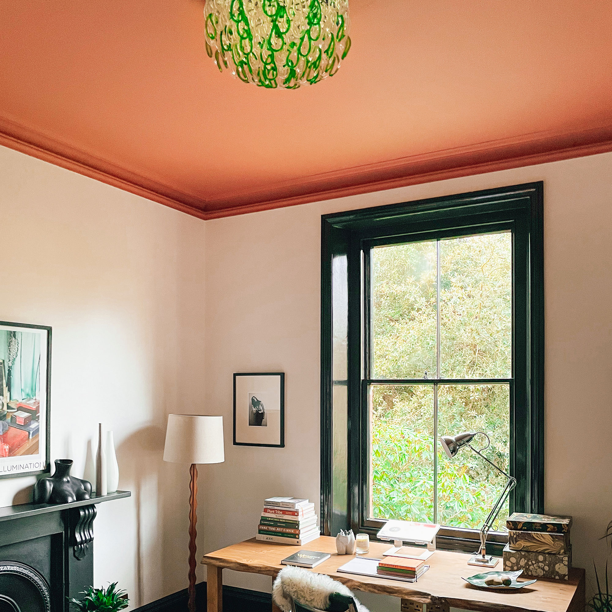 Home office with desk, decorated with white walls, black window frame, terracotta ceiling and green and glass chandelier 