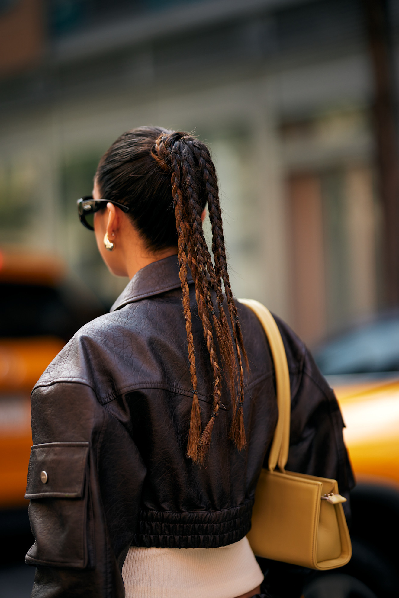 a woman in a brown leather jacket from the back with a multi-strand braided ponytail